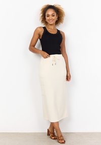 Schwarzes geripptes Tanktop mit Spitzenbesatz, kombiniert mit einem cremefarbenen Midirock mit Kordelzugbund und Seitentaschen. Braune Riemchen-Heels runden das Outfit ab.