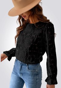 Zwarte kant blouson met bloemenpatroon, lange mouwen en gerimpelde manchetten, gecombineerd met lichtblauwe high-waisted jeans.