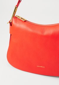 Borsa a tracolla in pelle rossa con una finitura morbida e testurizzata, forma curva, accessori in oro e chiusura con zip. Logo elegantemente impresso in oro.