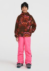 Pull en polaire avec un motif floral marron, rose et orange ; associé à un pantalon rose vif et un bonnet d'hiver noir.