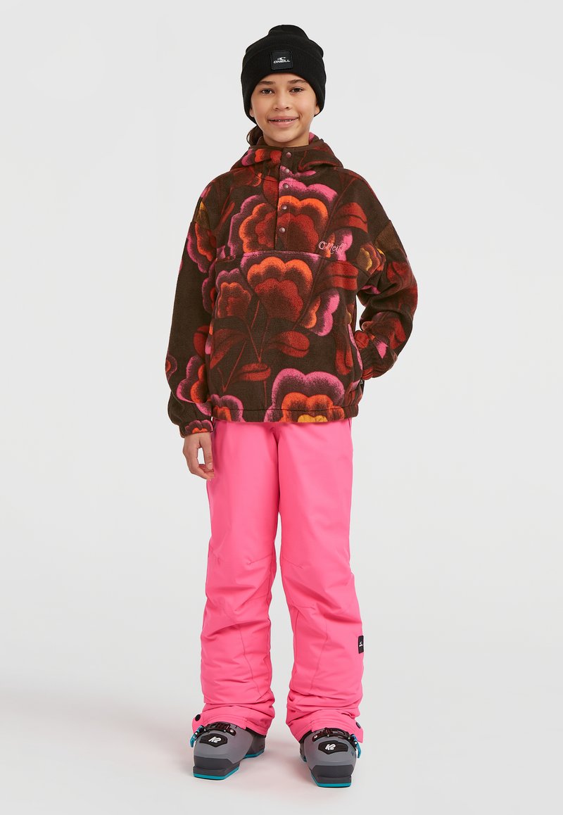 Pull en polaire avec un motif floral marron, rose et orange ; associé à un pantalon rose vif et un bonnet d'hiver noir.