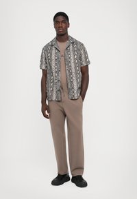 Kortermet skjorte med et slangeprint i grått og svart, parret med beige bukser med snor og svarte joggesko.