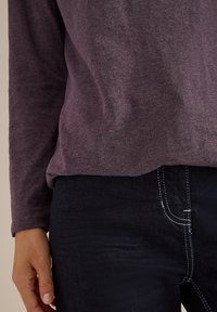 Czarna, długorękawowa koszula w ciemnopurpurowym kolorze, uszyta z miękkiej tkaniny, w połączeniu z czarnymi dżinsami z białymi przeszyciami i dopasowanym krojem.