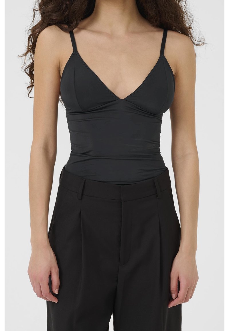 Débardeur noir à encolure en V profonde, bretelles fines et coupe ajustée, associé à un pantalon noir taille haute avec plis.