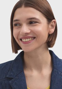 Tamno plava traper jakna s odrezanim reverima, uskim ovratnikom i teksturiranom površinom. Model ima kratku smeđu kosu i blagi osmijeh.