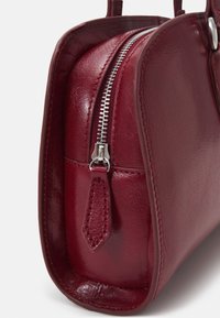 Gros plan d'un coin de sac à main en cuir bordeaux avec une fermeture éclair argentée et une tirette en cuir assortie.