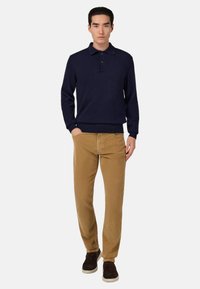 Polo shirt a maniche lunghe in maglia di colore navy, con due bottoni sul colletto, abbinato a pantaloni in velluto a coste color beige; modello che indossa scarpe marrone scuro.