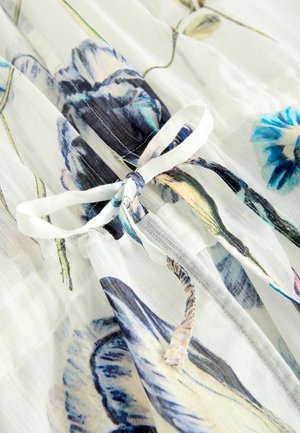 Kangas chiffon berbunga memiliki latar belakang putih dengan pola bunga biru dan ungu. Detail tali di pinggang menunjukkan tekstur yang ringan dan nyaman.