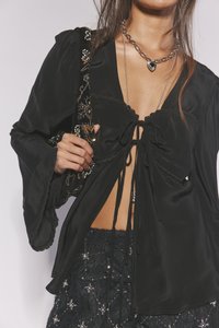 Crna svilena bluza s dubokim V-izrezom i detaljem kravate sprijeda, sa širokim rukavima i nazubljenim rubom. Uz nju ide torbica ukrašena perlicama.