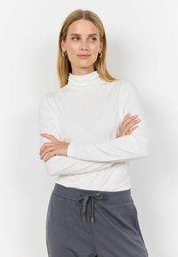 Bílý dlouhý rukáv rolák z lehkého materiálu, spárovaný se šedými kalhotami na stažení s uvolněným střihem a hladkou texturou.