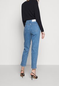 Jeans de tiro alto de color azul claro con pierna recta, cinco bolsillos y una etiqueta blanca en la parte trasera. Combinados con sandalias de tacón negras.