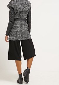 Grau melierter Mantel mit Kapuze und schwarzen Lederärmeln, tailliert mit einem Gürtel, kombiniert mit schwarzen Culottes und Ankle Boots. Strukturiertes Material.