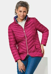 Roze pufferjack met zigzagstiksel, volledige rits, hoge kraag en blauwe binnenvoering. Beschikt over een getailleerd ontwerp en zijzakken.