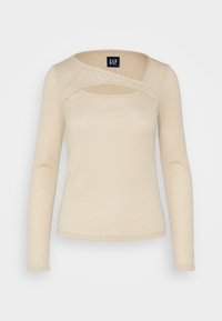 Haut beige à manches longues avec une finition texturée. Présente un design original avec une découpe au niveau du col et une silhouette lisse et ajustée.