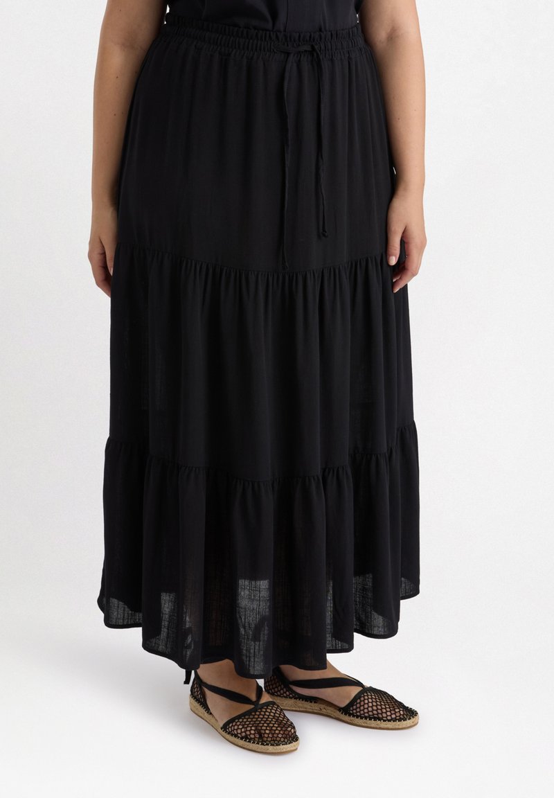 Gonna maxi nera a strati con elastico in vita e cordoncino. Indossata con espadrillas nere con punta aperta caratterizzate da un design in rete.