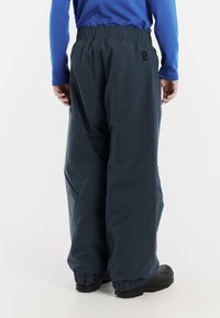 Mörkblå vattentäta byxor med elastisk midja, lös passform, förstärkta mudd och justerbara tryckknappar, tillsammans med svarta stövlar.