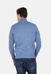 Maglione blu lavorato a maglia con colletto alto e polsini a coste, che mostra una texture liscia e un design aderente, abbinato a jeans in denim.