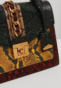 Bolso de mano con estampado de serpiente multicolor y herrajes dorados, que cuenta con una asa de cadena gruesa y un diseño estructurado. Los colores incluyen verde, amarillo, rojo y negro.
