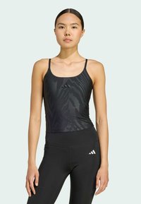 Zwarte sportieve tanktop met dunne bandjes en een subtiel zebra patroon, gecombineerd met hoge zwarte leggings die een logo-accent tonen.