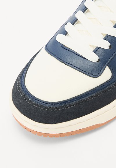 Zapatilla azul y crema con upper de cuero liso y ante texturizado, cordones blancos y suela de goma. Punta redonda y detalles de costura.