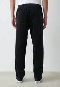 Black corduroy pants with a relaxed fit, featuring a drawstring waist and two back pockets, paired with dark sneakers.