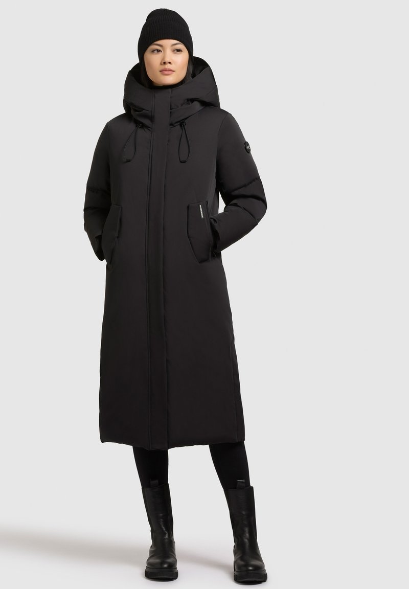 Černý zateplený dlouhý kabát s kapucí, předním zipem, stahovacími šňůrkami a bočními kapsami. Hladká textura, rovný střih a minimalistický design.