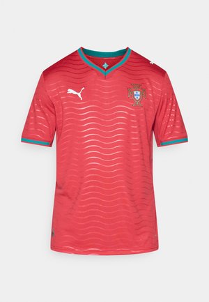 Raudonas futbolo marškinėlis su V formos iškirpte, trumpomis rankovėmis ir banguotu raštu. Priekyje yra turkio spalvos akcentai ir Portugalijos nacionalinis emblemė.