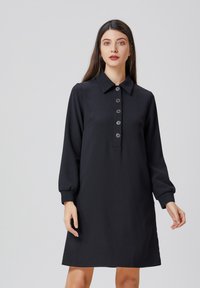 Robe noire à manches longues avec un col, patte de boutonnage à cinq boutons et poignets élastiques ; tissu lisse avec une coupe droite et décontractée.