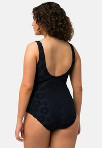Marineblauwe ééndelige zwemoutfit met een lage rug, dikke banden en een bloemenstructuur. Stof lijkt glad en elastisch te zijn.