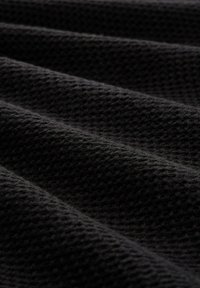 Schwarzer Stoff mit texturierter Waffelstruktur, der gefaltete Wellen zeigt, die seine Dicke und weiche Textur betonen.
