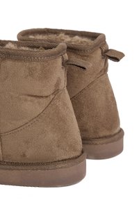 Stivaletti ankle in suede marrone con morbido rivestimento in pelliccia sintetica e linguette sul retro. Suola in gomma piatta e semplice dettagli cuciti.