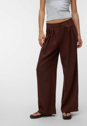 Modèle portant un pantalon large marron à fines rayures avec des plis et taille haute, associé à un crop top gris clair et des sandales noires.