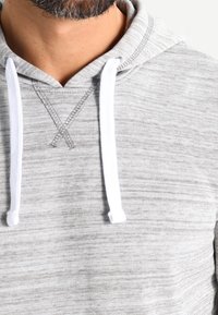 Sudadera con capucha gris con cordones blancos, que presenta una tela texturizada, un patrón de puntadas cruzadas en el cuello y un ajuste holgado.