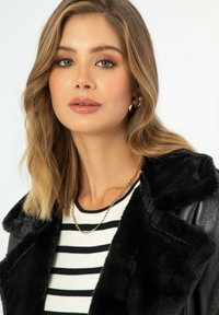 Giacca con colletto in pelliccia sintetica nera sopra una camicia a righe bianche e nere, accessoriamoci con una collana in oro e orecchini a cerchio.
