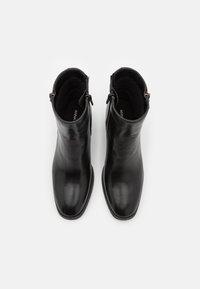 Botas de cuero negras hasta el tobillo con un diseño elegante, punta afilada y cierre de cremallera en el lateral. Textura suave y perfil minimalista.