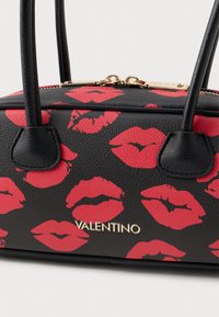 Borsa a mano in pelle nera con impronte labbra rosse, hardware dorato, doppi manici superiori e chiusura con zip. Presenta il marchio sulla parte anteriore.