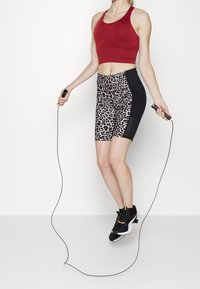 Czerony stanik sportowy w połączeniu z czarno-leopardowymi szortami z wysokim stanem. Czarne buty sportowe z białymi i złotymi akcentami. Skakanka w ręku.