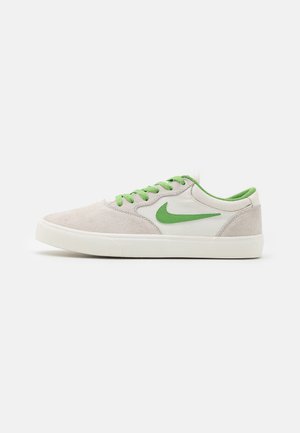 Beiger Sneaker in niedriger Ausführung mit grünen Schnürsenkeln, grünem Nike Swoosh-Logo und weißer Sohle auf einfachem weißem Hintergrund.