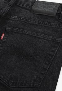 Jeans de denim negro con una superficie texturizada, diseño clásico de cinco bolsillos, etiqueta roja en el bolsillo trasero y una parche de cuero con marca.