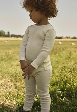 Haut à manches longues en tricot côtelé de couleur crème et leggings, présentant une coupe ajustée et une texture douce, portés par un enfant à l'extérieur sur l'herbe.