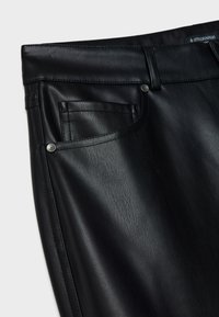 Pantalons en faux cuir noir présentant des détails tels que des poches avant, des passants de ceinture et des rivets en métal sur un tissu à texture lisse.