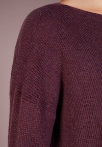 Burgundy stickad tröja med ribbad textur, lätt båtformad halsringning och lös passform. Har breda ärmar och en sömlös övergång till kroppen.