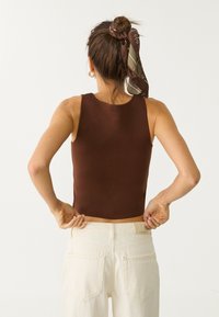 Top in maglia a coste marrone abbinato a jeans a vita alta color crema, che evidenziano un design aderente e una costruzione senza soluzione di continuità.