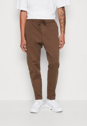 Bruine katoenbroek met een elastische tailleband, trekkoord en zijzakken, gecombineerd met witte sneakers. Soepele textuur en taps toelopende pasvorm.