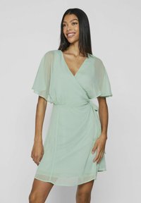 Mäta zelené oblečenie s krátkymi flitrovými rukávmi, V-výstrihom a viazaním v páse. Vyrobené z ľahkej, texturovanej tkaniny.