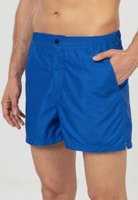 Blauwe zwembroek van lichtgewicht stof, met een zwart abstract patroon, elastische tailleband en zijzakken.