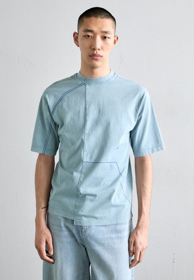 Lichtblauwe t-shirt met korte mouwen, featuring contrasterende blauwe stiksels en een uniek naai ontwerp, gemaakt van zachte katoen.