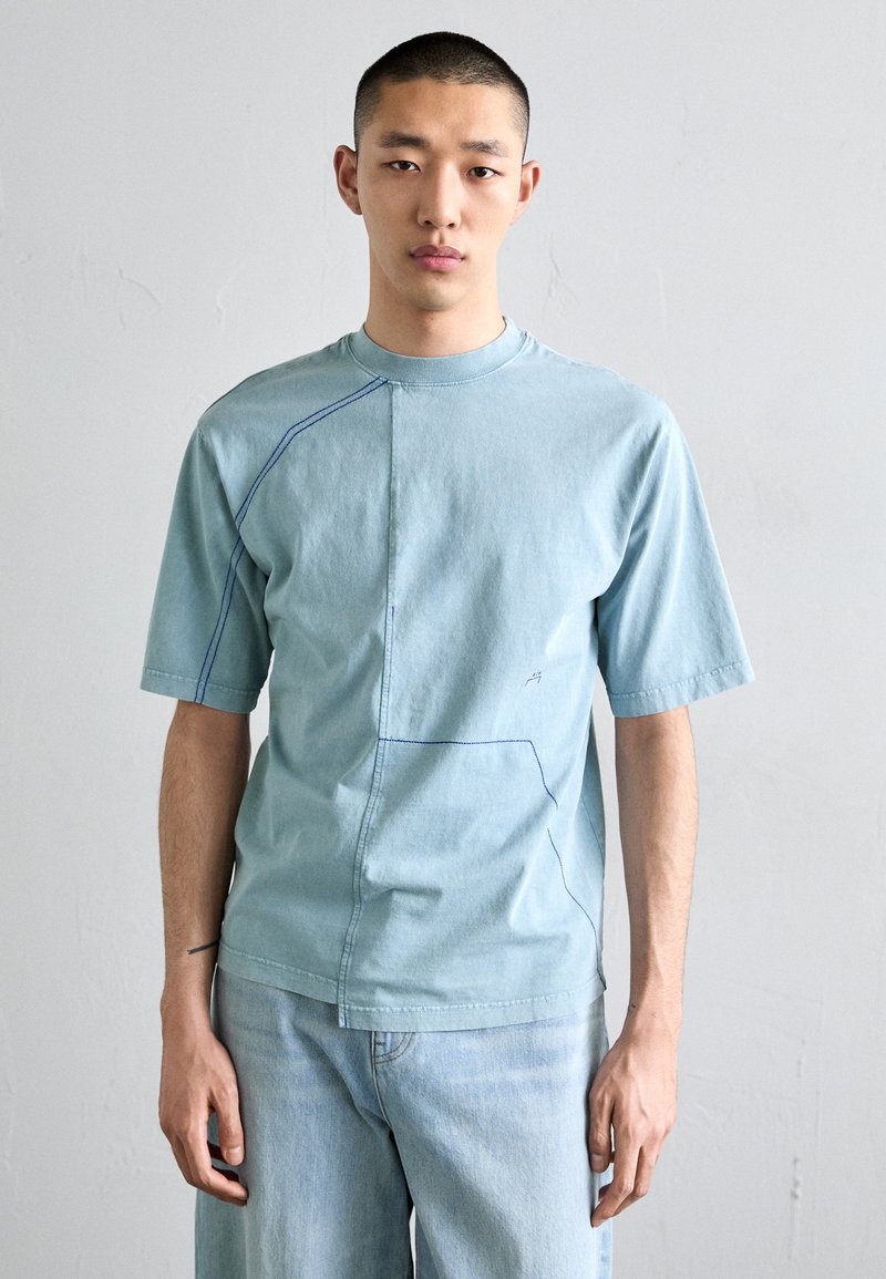T-shirt bleu clair à manches courtes avec des coutures bleues contrastantes et un design de couture unique, fabriqué en tissu en coton doux.