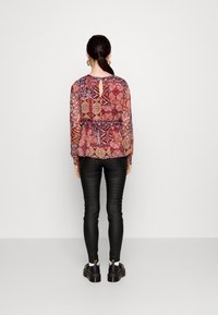 Blusa a maniche lunghe con motivo multicolore, scollo rotondo e dettaglio a chiave sulla schiena, abbinata a pantaloni in pelle neri e scarpe.