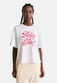 Camiseta de algodón blanca de manga corta, con un gráfico en negrita de color rosa que dice "Tómalo con calma" en diseño a rayas. Corte relajado con cuello redondo.